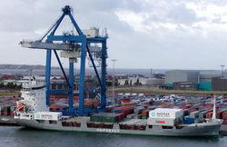 Container ship "Rita" being loaded at Copenhagen; note crew standing on deck, and stacks of containers on shore.